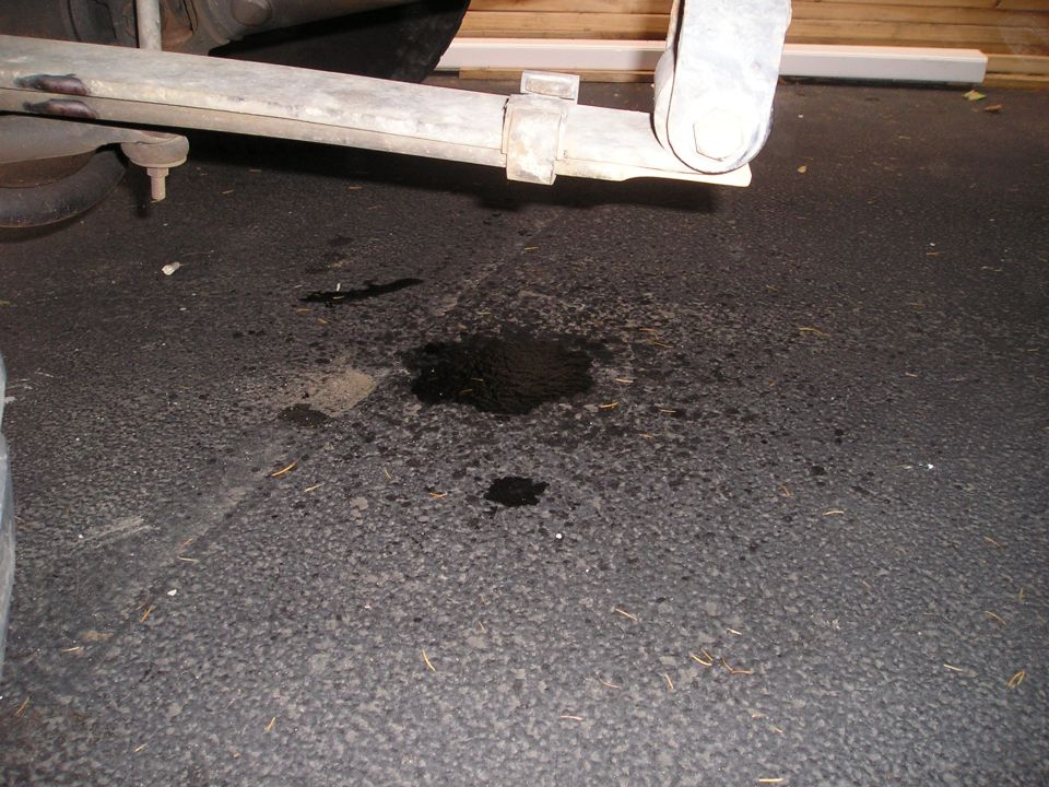 Undercarriage of a vehicle with a fluid leak on asphalt. Leaf spring visible
