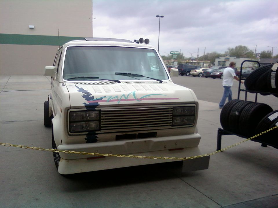 White van with a colorful stripe decal on the hood, parked in front of a building