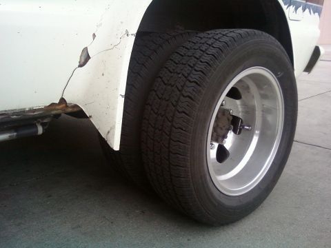 2000 Mercury Grand Marquis - The rear wheel assembly of a vehicle shows dual tires and a silver rim, with visible body damage.