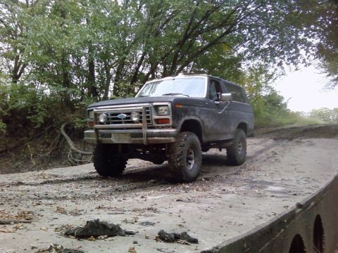1986 Ford Bronco - This black Ford Bronco is shown off-road, equipped with large tires for rough terrain.