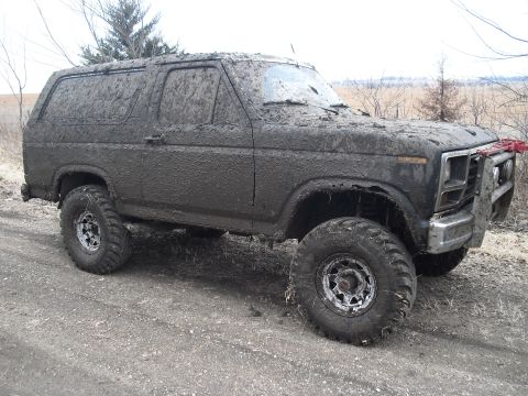 1986 Ford Bronco - This heavily mud-covered SUV is viewed from the front three-quarter angle, obscuring any specific year-defining details.