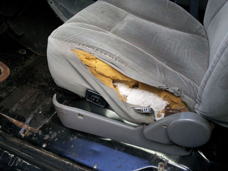 Torn gray fabric car seat with exposed yellow foam and white stuffing, showing a "LIFT" lever