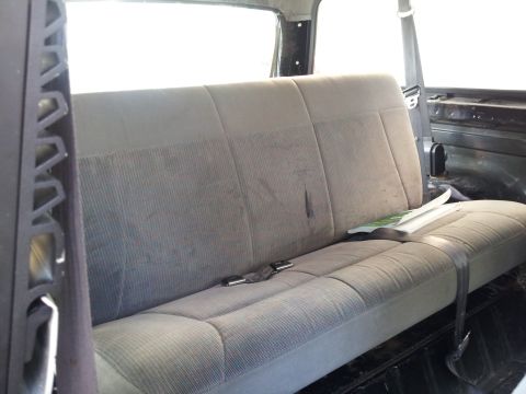 1995 Ford Bronco - Interior view of a rear bench seat, showing the fabric upholstery and seatbelts. A magazine rests on the seat.