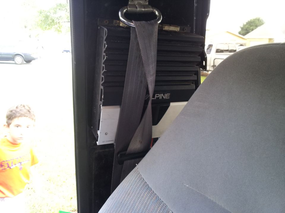 Car interior showing an Alpine amplifier mounted behind a seatbelt, with a child visible through the window