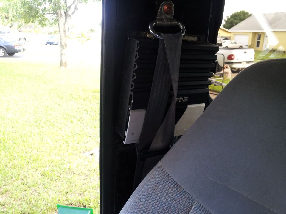 Interior shot showing a seatbelt, an Alpine amplifier, and a view out the window to a parked car and a pickup truck