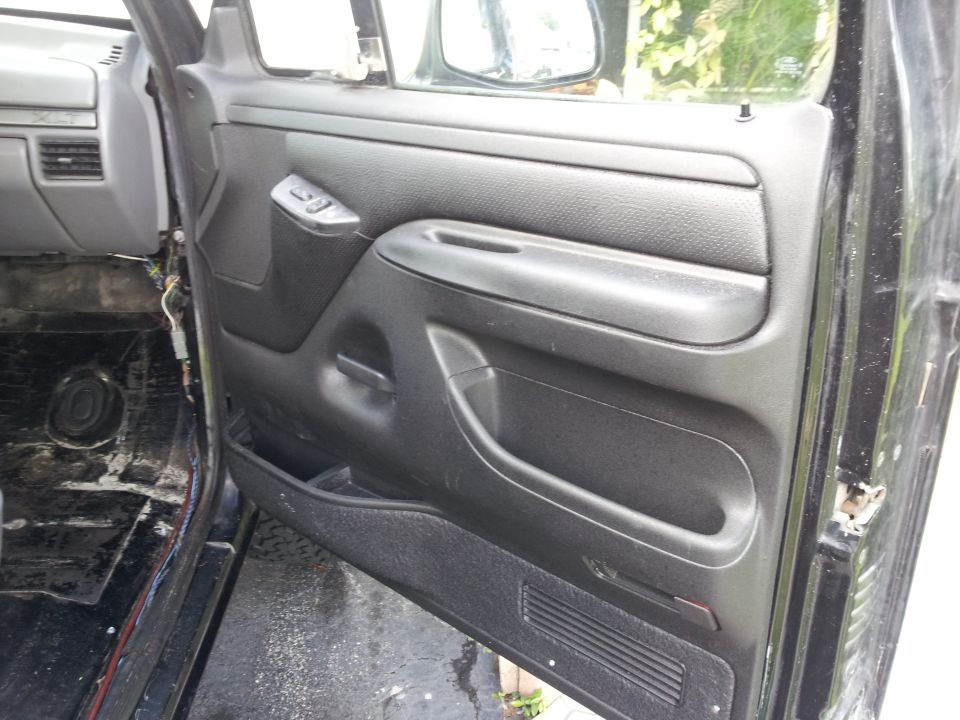 Black interior door panel with armrest and window controls, showing exposed wiring and bare floor