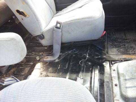 1995 Ford Bronco - Worn interior of a vehicle with visible seatbelt hardware and a dirty floor.
