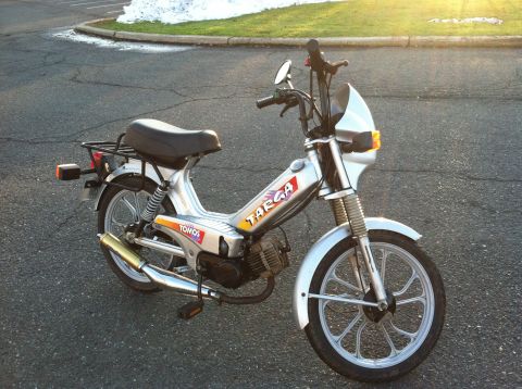 1999 Tomos Targa - A silver Tomos Targa moped is parked on a paved surface with a grassy area and some snow visible in the background.