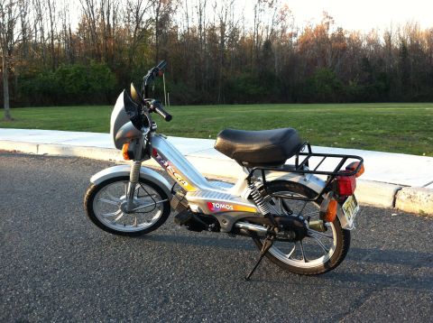 1999 Tomos Targa - A silver moped is parked on the side of a road with trees in the background.