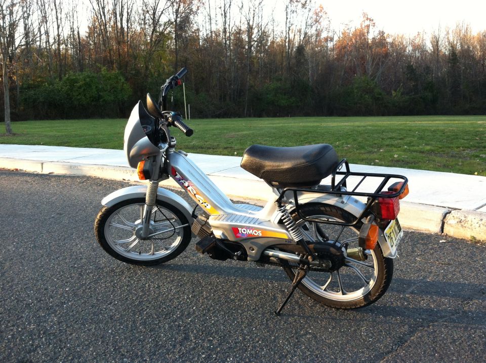 Silver moped with black seat and rack, parked on asphalt
