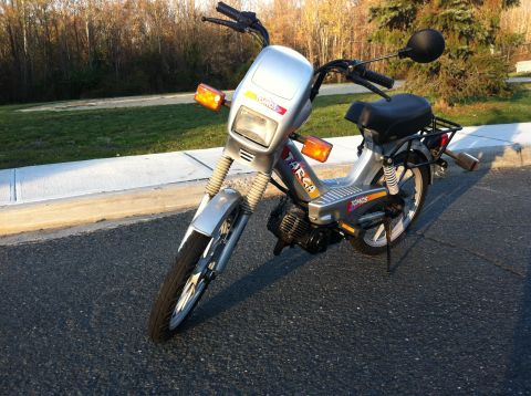 1999 Tomos Targa - A silver moped, possibly a Tomos Targa, is parked on an asphalt surface with a grassy area and trees in the background.