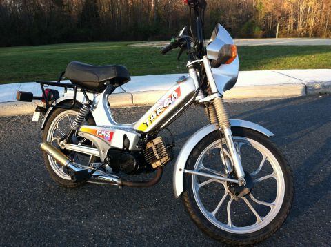 1999 Tomos Targa - A silver Tomos moped is parked on an asphalt surface with a grassy area and trees in the background.