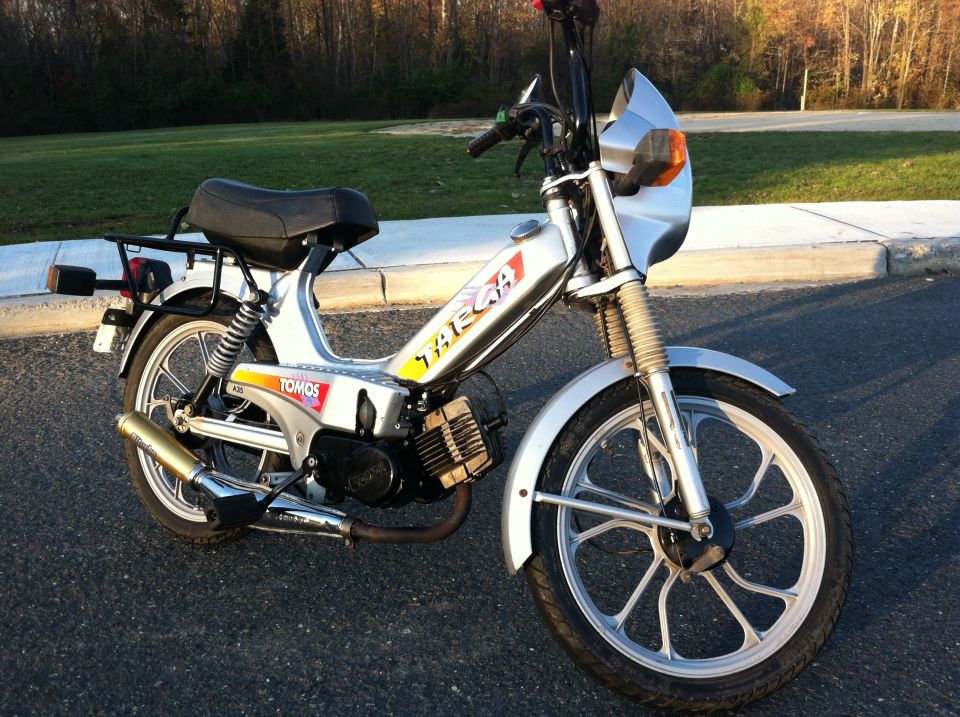 Silver Tomos moped with yellow and red stripes on the frame. It has a small silver fairing