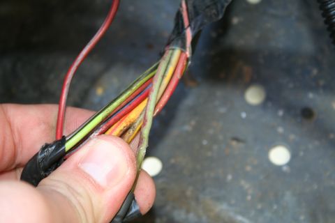 1982 Ford Bronco - A hand inspects a damaged wiring harness, revealing multiple colored wires that appear to be frayed and exposed.