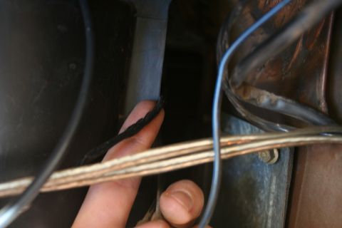 1982 Ford Bronco - A finger points to a frayed wire within a vehicle's wiring harness, suggesting a potential electrical issue.