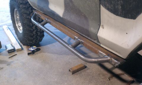 1990 Ford Bronco - Custom rock sliders installed on the side of a vehicle, with a large tire and workshop floor visible.