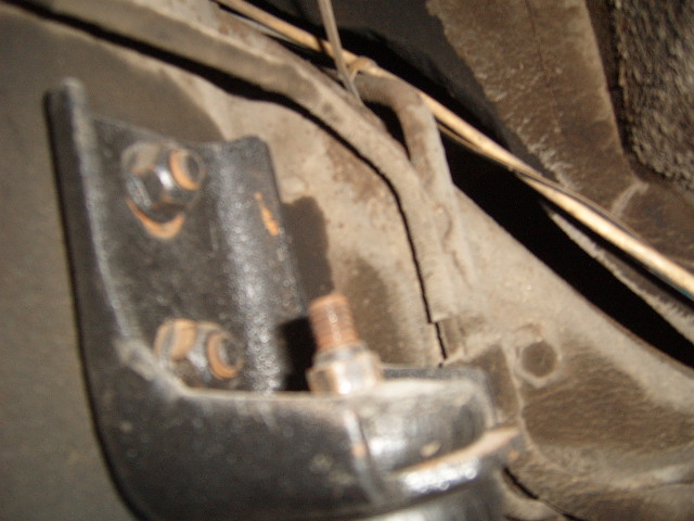Close-up of a rusty metal bracket with bolts attached to a vehicle's undercarriage