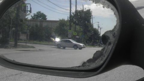 1989 Ford Bronco - A silver sedan is captured in the side mirror as it makes a turn at an intersection on a sunny day.