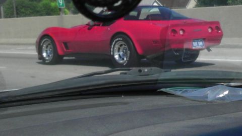 1989 Ford Bronco - A red sports car drives on the highway, seen from behind.