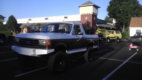 1989 Ford Bronco - A lifted two-tone pickup truck is parked in a lot with other vehicles present.