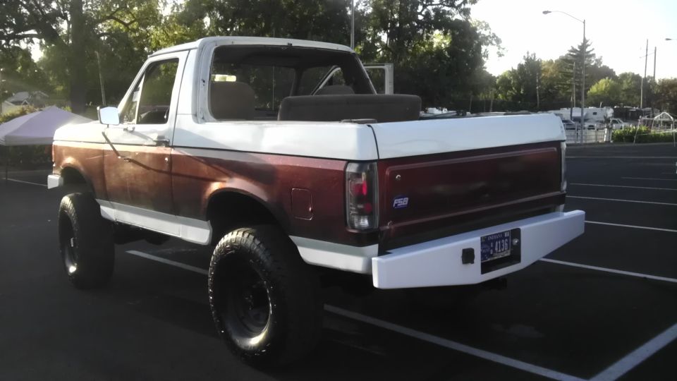 White and maroon Ford Bronco with aftermarket bumper and large tires, viewed from the rear