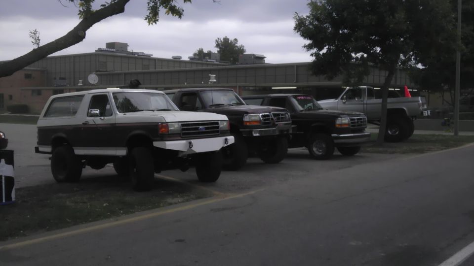 1989 Ford Bronco with aftermarket bumper, parked next to three Ford trucks