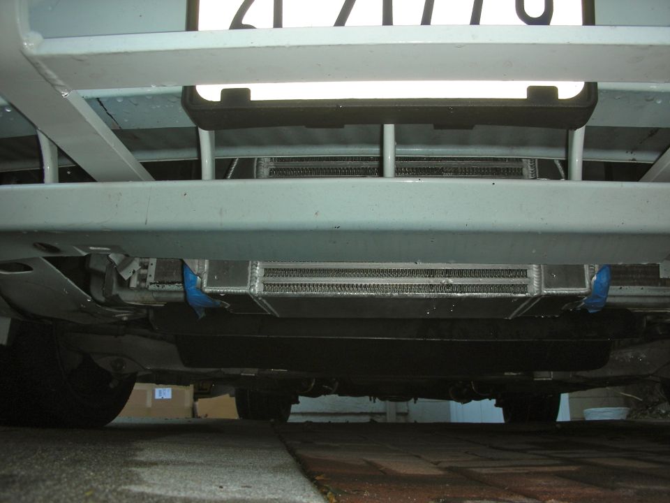 Undercarriage view of a vehicle showing an aftermarket supercharger system and part of a license plate
