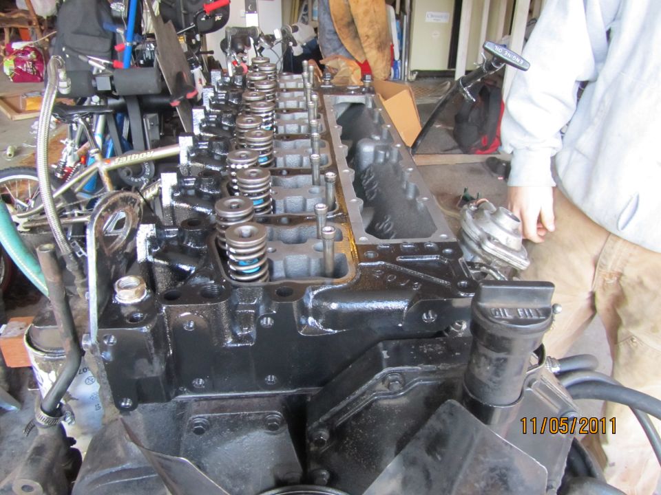 Black engine block with visible valves and springs, in a garage setting