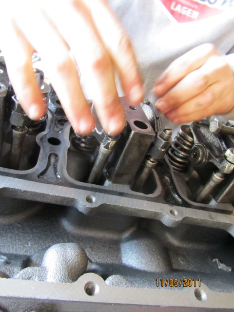 1984 Ford Bronco - Close-up of engine internals with hands adjusting fuel injectors and valve train components.