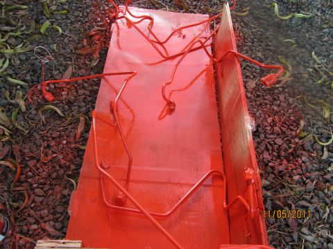 1984 Ford Bronco - Red painted metal tubes are laid out on a wooden board, possibly for a vehicle repair or modification.