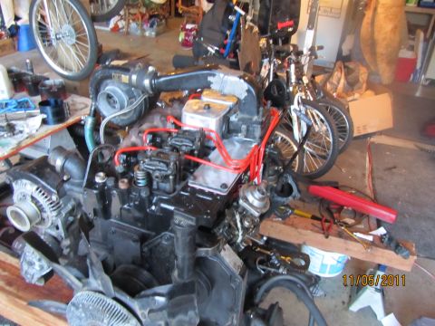1984 Ford Bronco - A disassembled diesel engine sits on a wooden platform in a cluttered garage, with bicycles in the background.