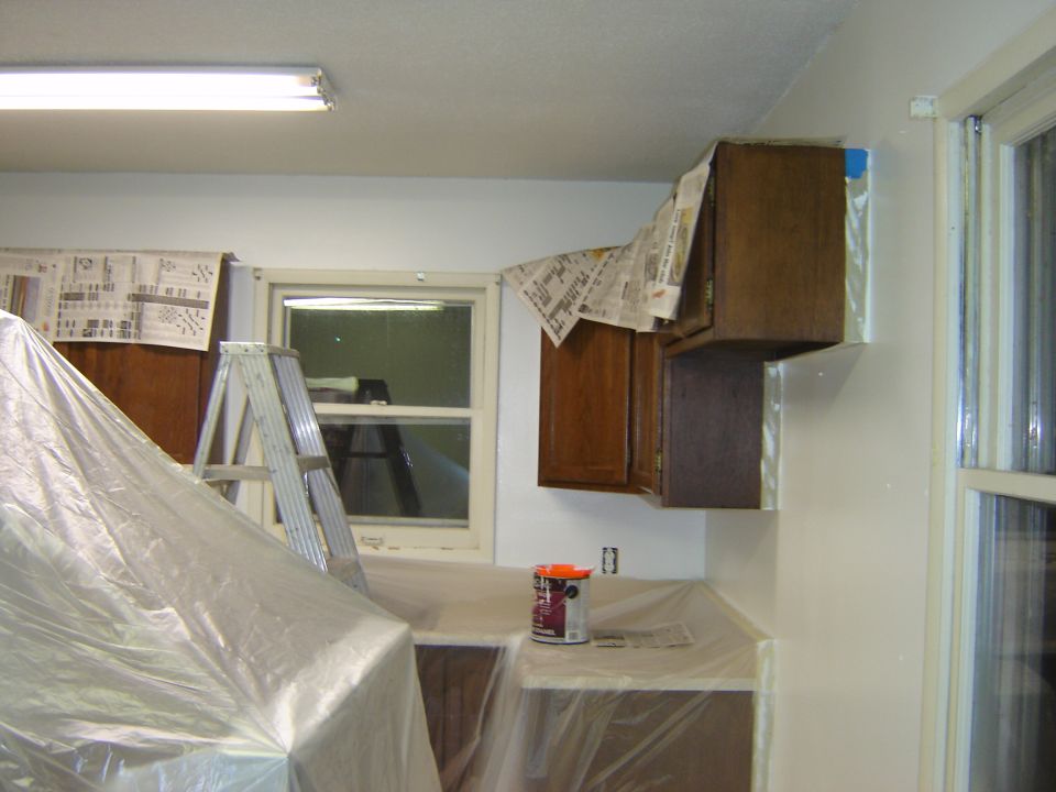 Kitchen undergoing renovation with cabinets covered in plastic, a ladder, and paint cans on the counter