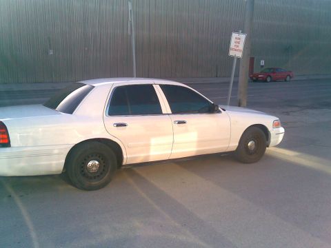 2001 Ford Crown Victoria - A white 2001 Ford Crown Victoria sedan is parked on an asphalt surface, with another red car visible in the background.