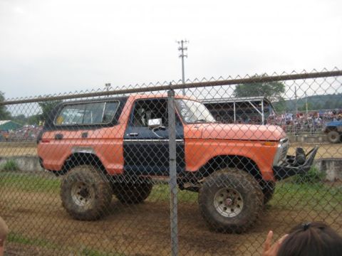 1978 Ford Bronco - This modified 1978 Ford Bronco is seen from the side, partially obscured by a fence, with a crowd in the background.