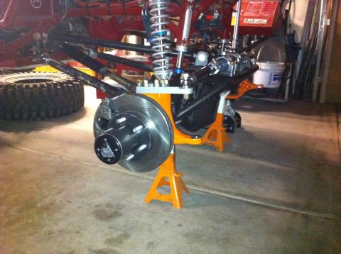 Suzuki Samurai - Front axle assembly with disc brake and coilover shock, supported by jack stands in a garage.