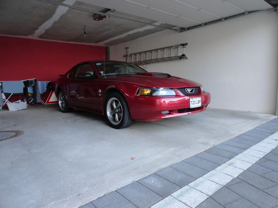 Red Ford Mustang coupe parked in a garage, front 3/4 view. Visible license plate T23 LBP