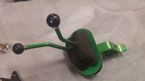 1979 Ford Bronco - A green dual-lever shifter assembly with black knobs is shown on a gray surface.