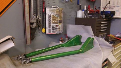 1979 Ford Bronco - Green suspension control arms with rod ends sit on a workbench next to tools.