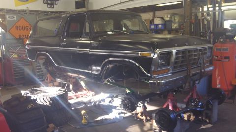 1979 Ford Bronco - A black Ford Bronco is elevated on jack stands in a workshop, undergoing repairs or modifications.