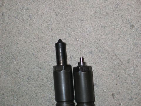 1984 Ford Bronco - Two diesel injectors are shown against a concrete surface, with one injector appearing larger than the other.