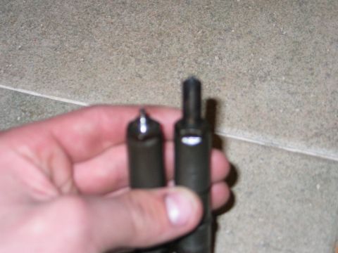 1984 Ford Bronco - A hand holds two diesel injector nozzles, one with a pointed tip and the other with a flat tip.