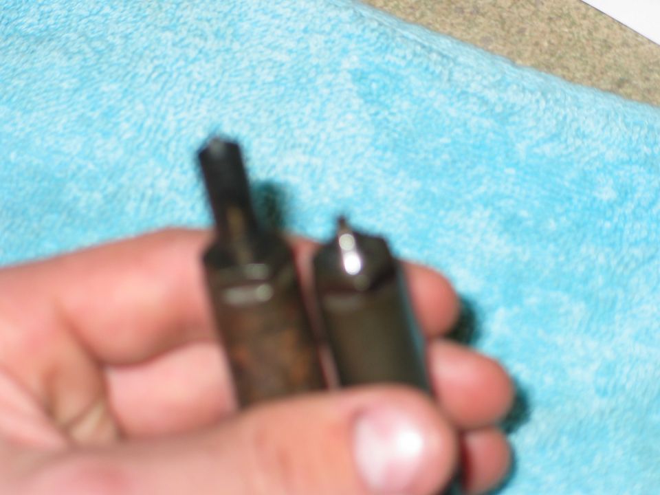 Hand holding two fuel injectors, one is darker and appears older than the other