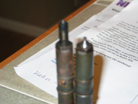 1984 Ford Bronco - Two fuel injectors are shown on a table with some documents in the background.
