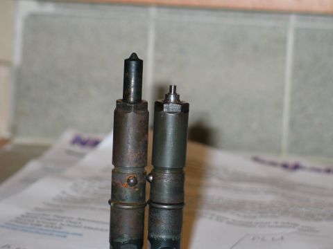 1984 Ford Bronco - Two fuel injectors are shown, one with a pointed tip and the other with a smaller top, placed on top of some documents.
