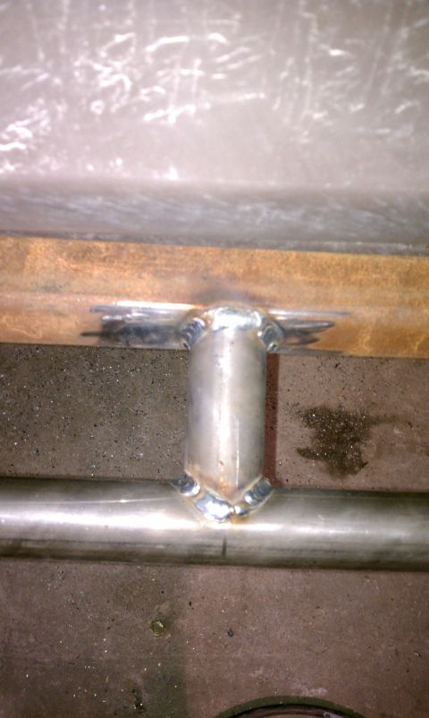 1979 Ford Bronco - Close-up of a welded metal bracket on a pipe, with a rusty beam overhead.