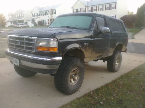 1995 Ford Bronco - This lifted Ford Bronco is parked on a driveway, showing off its off-road tires and dirty exterior.