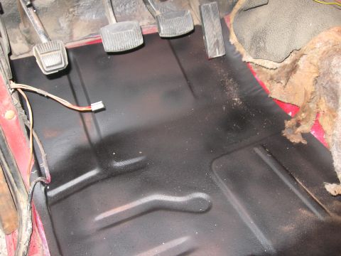 1981 Ford Bronco - The interior floor of a vehicle shows pedals, wiring, and a newly coated black floor pan.
