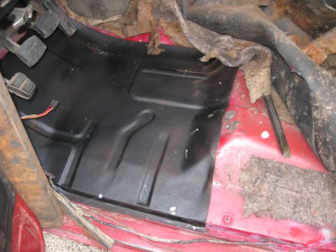 1981 Ford Bronco - The interior floor of a vehicle shows a newly installed black metal panel with exposed red metal and insulation.