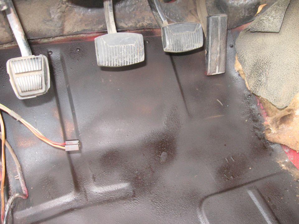 Vehicle interior floor showing clutch, brake, and accelerator pedals. Wiring harness visible near the left pedal