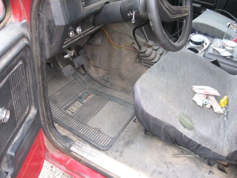1981 Ford Bronco - The interior of a 1981 Ford Bronco, floor mats with the Ford logo, pedals, steering wheel, and a worn seat.